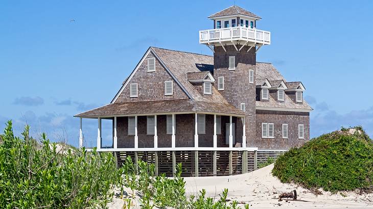 A brown building with a tower, surrounded by blue sky, sand dunes and bushes