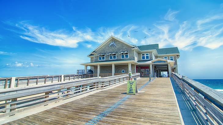 Wooden boardwalk leading to a building overlooking the sea on a sunny day