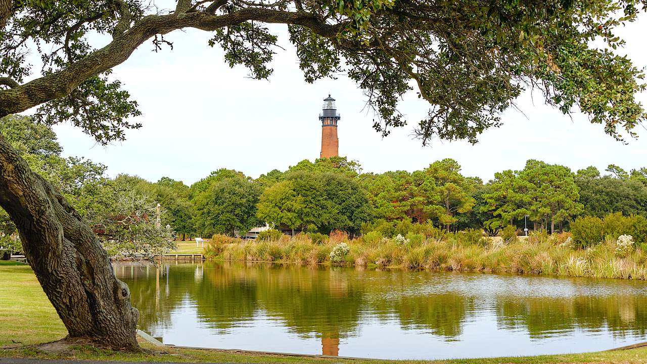 A red lighthouse in the background facing bushy green trees and a still body of water