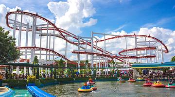 Side view of a rollercoaster's white and red rail and a pool with people on floaters