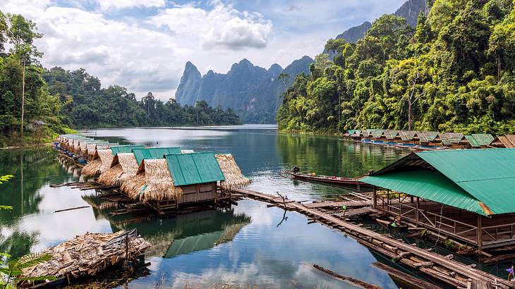 A lake with trees and mountains in the background and a row of floating huts in front