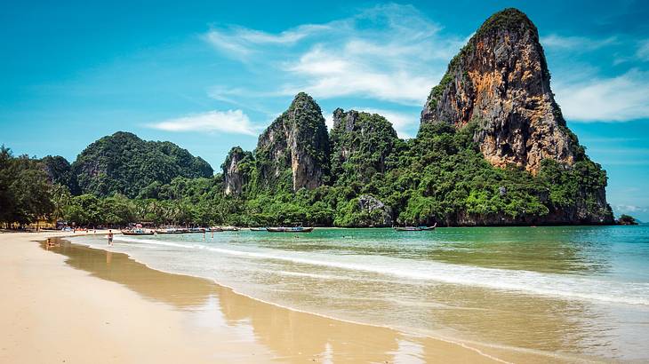 View of a beach with people, boats, and high limestone cliffs covered with trees View of a beach with people, boats, and high limestone cliffs covered with trees