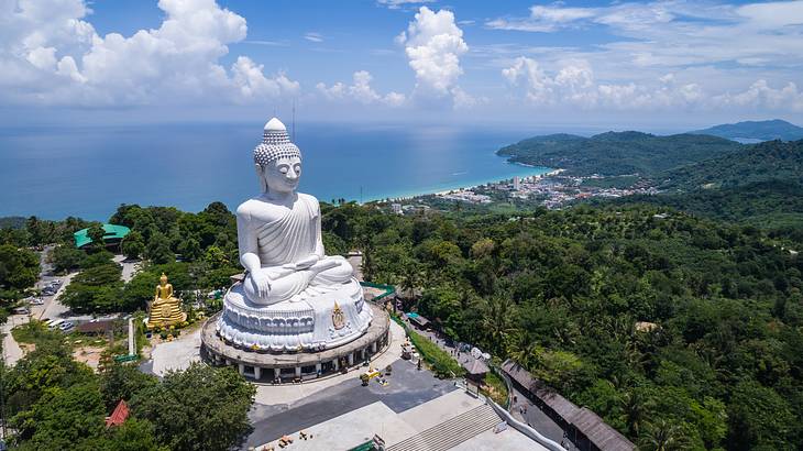 Aerial view of a big Buddha statue surrounded by trees, buildings, and the ocean Aerial view of a big Buddha statue surrounded by trees, buildings, and the ocean