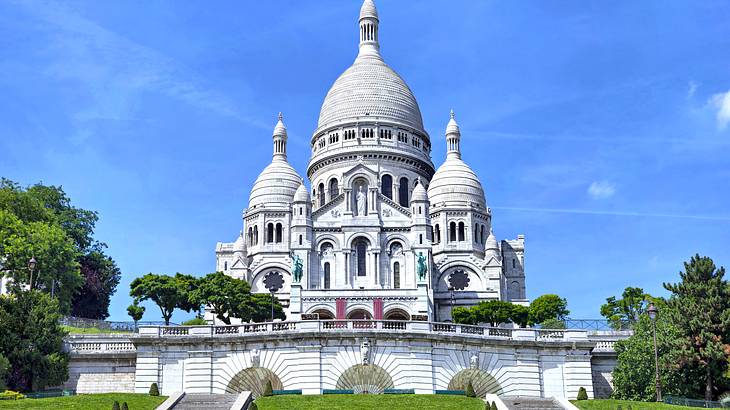 A white three-domed Catholic church against a blue sky surrounded by trees