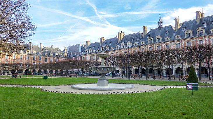 An old building surrounded by bare trees, a green lawn, and a fountain