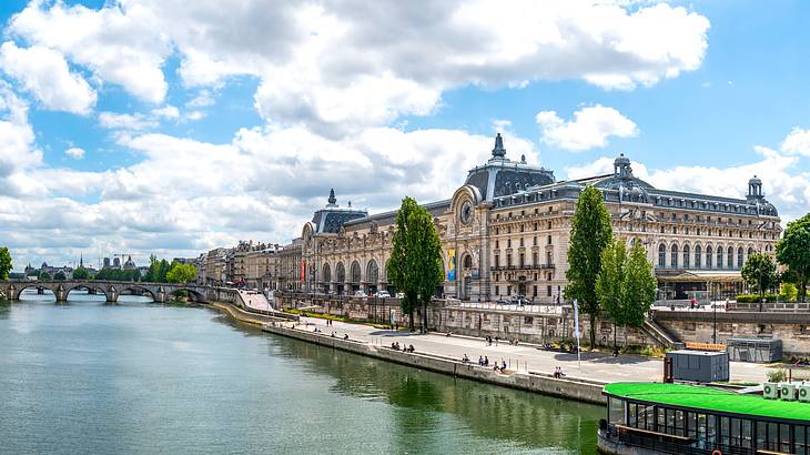 A massive building with trees in front facing a river with a boat