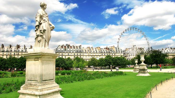 A garden with a statue, Ferris wheel, bushes, and trees under a blue sky