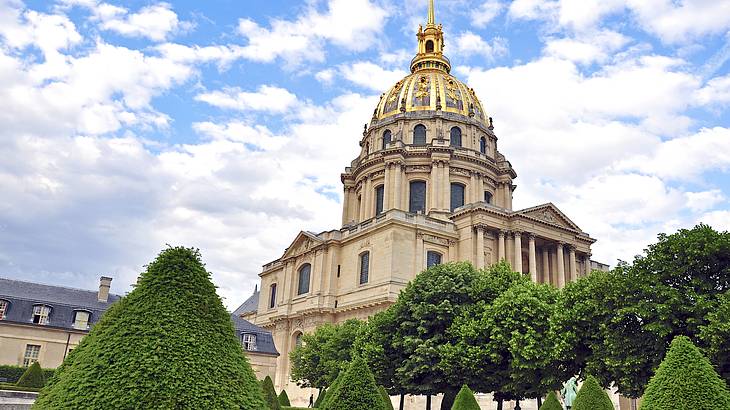 A museum building with a dome on top and a manicured lawn in front under a cloudy sky