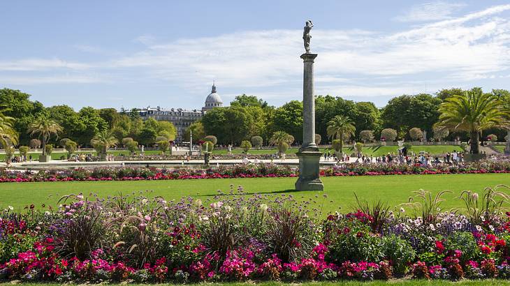 Landscape view of a colourful garden with flowers, trees, and monument on a sunny day