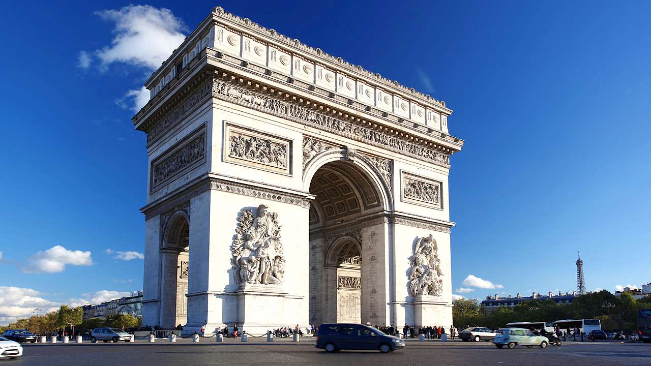 A large monumental arch standing beneath a blue sky with cars going around it