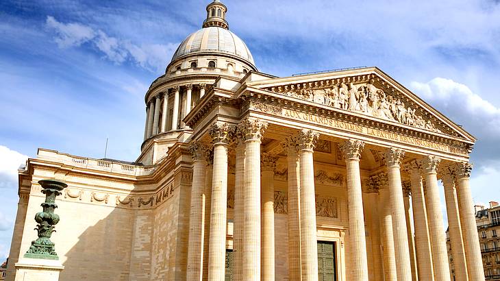 The exterior of a grand building with a dome and columns on a sunny day