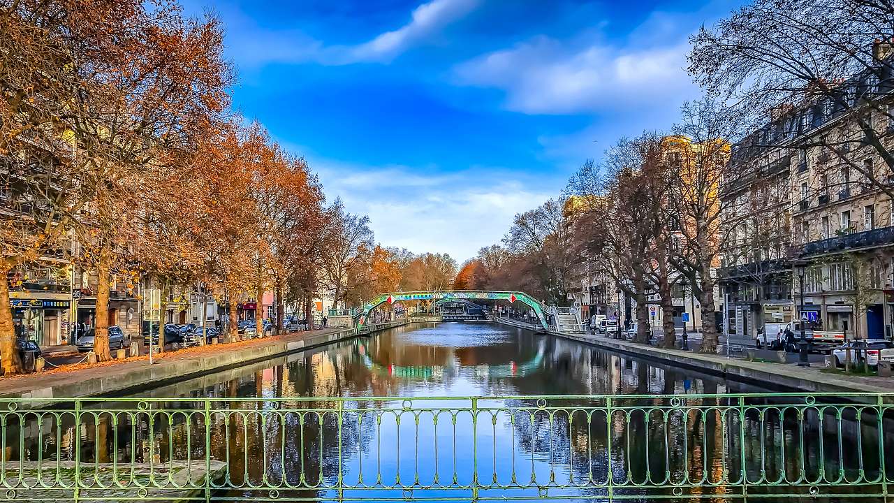 A canal with a bridge surrounded by trees in autumn colors with a fence in front