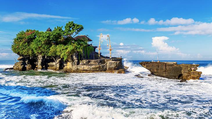 A temple on a rock with trees surrounded by more rocks and waves