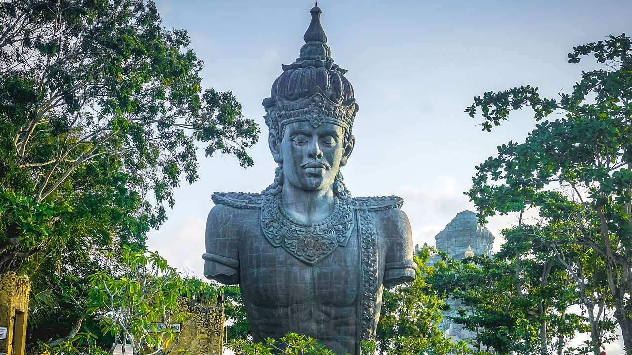 A huge statue of a Hindu god surrounded by green leafy trees