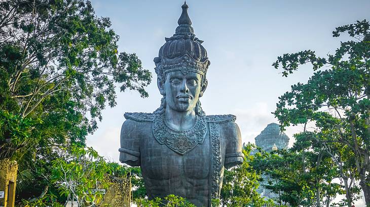 A huge statue of a Hindu god surrounded by green leafy trees