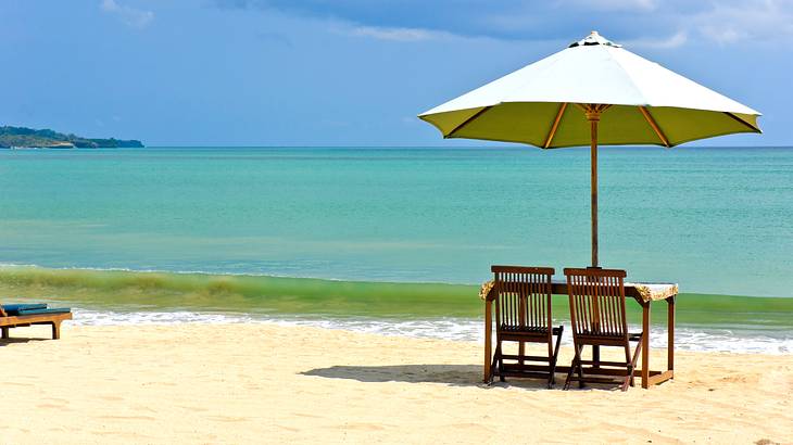 A white-sand beach with waves on a partly cloudy day with a beach umbrella and chairs