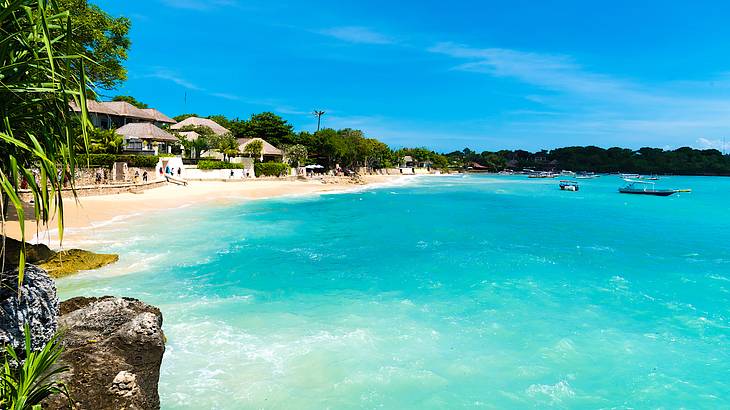 Boats on beautiful blue water and cottages on the white sandy beach on a clear day