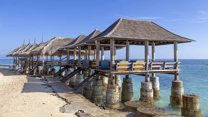 A row of huts standing in blue water with rocks in front