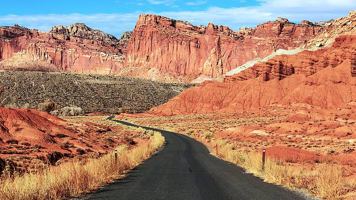 A paved road leading to red rocky cliffs at the back with blue sky above