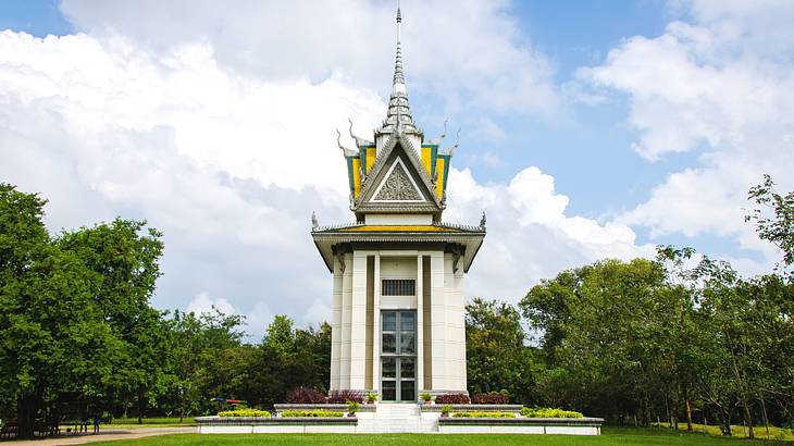 A small structure with glass windows and an ornate roof next to the grass and trees