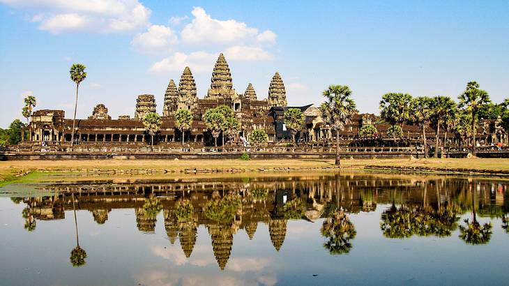 An ancient temple structure and trees reflected in a lake on a clear day