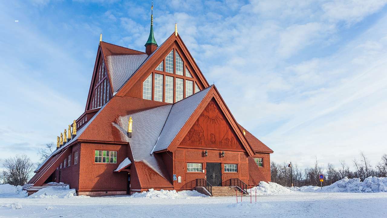 A wooden church structure surrounded by snow under a blue sky with clouds