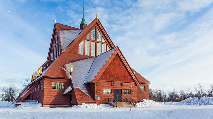 A wooden church structure surrounded by snow under a blue sky with clouds