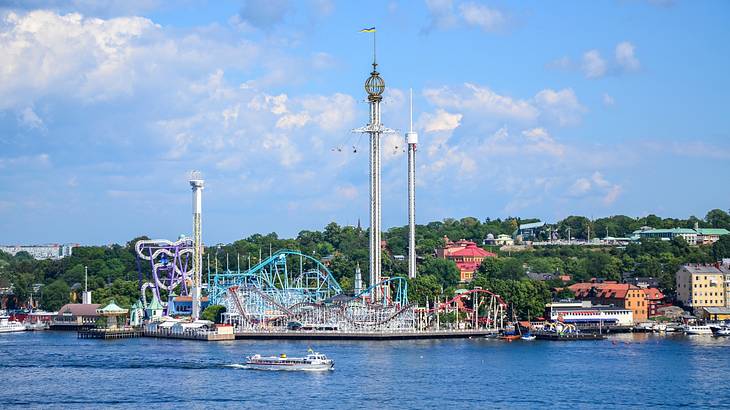 A theme park next to the water and green trees under a blue sky with some clouds