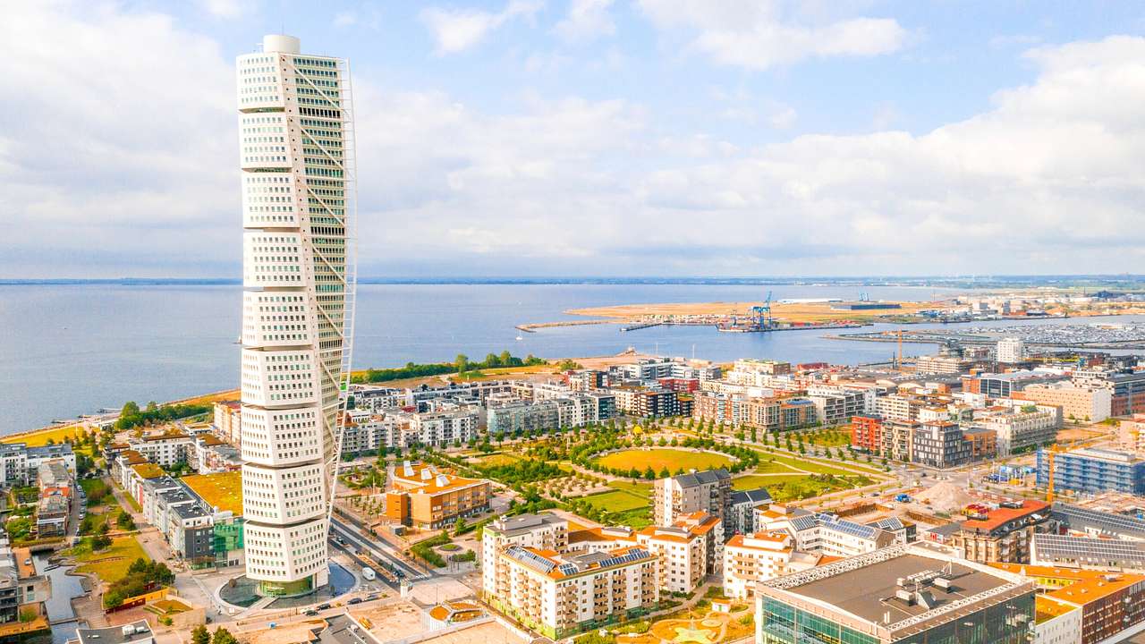 A modern twisting-style skyscraper surrounded by other buildings next to the water