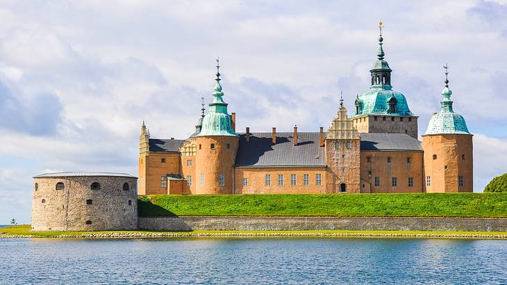 A castle structure with green roofs next to a body of water