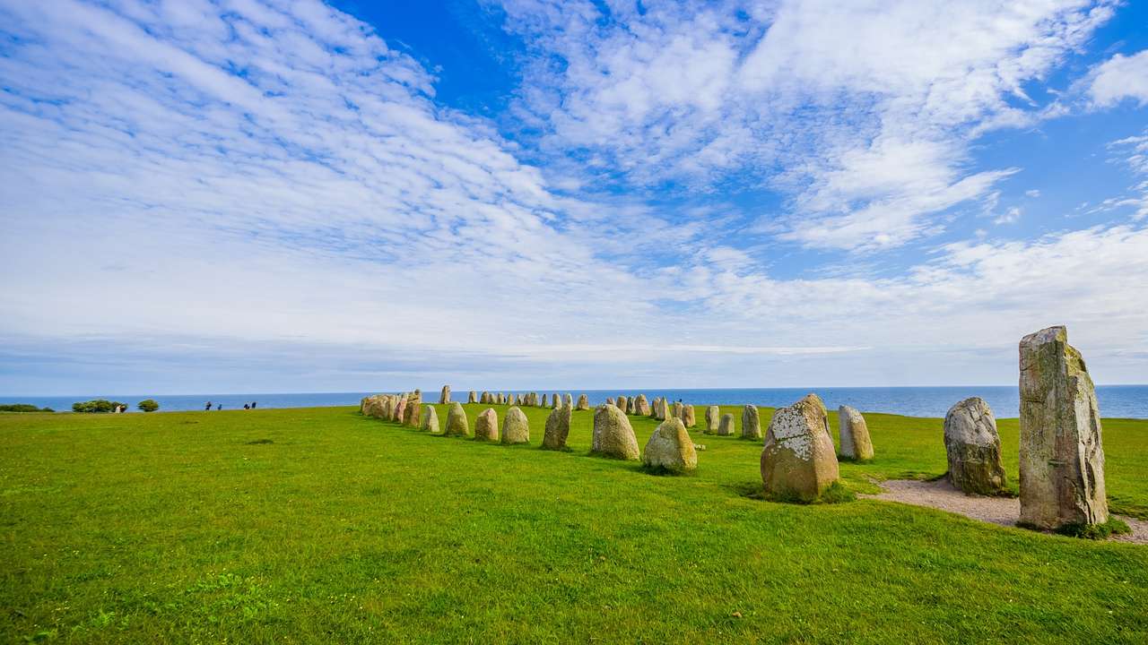 A circle of small boulders on the grass under a blue sky with clouds