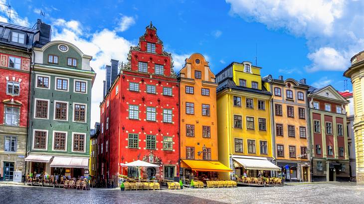 Brightly coloured European buildings in a square under a bright blue sky with clouds