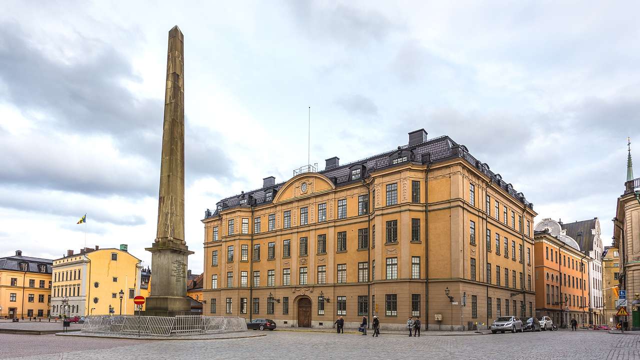 A stone obelisk in a square next to old European buildings under a grey cloudy sky