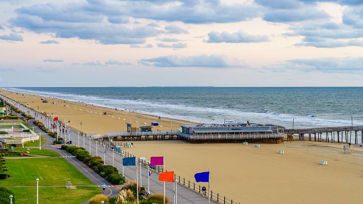 A sandy beach with a pier and a body of water with a walkway and colored flags A sandy beach with a pier and a body of water with a walkway and colored flags