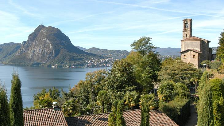 A body of water next to trees and a building, with a mountain in the background A body of water next to trees and a building, with a mountain in the background