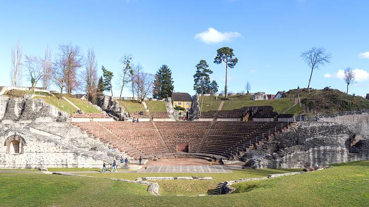 The ruins of an amphitheatre surrounded by grass and trees on a clear day