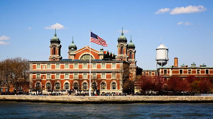 A red brick building under blue sky with an American flag and water in front A red brick building under blue sky with an American flag and water in front