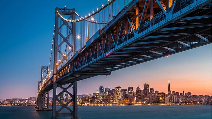 A suspension bridge over a bay with a skyline in the distance at night A suspension bridge over a bay with a skyline in the distance at night