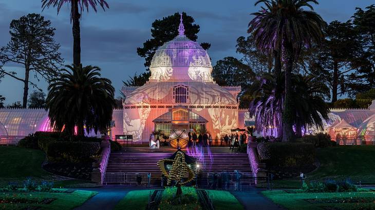 A conservatory with grass and palm trees surrounding it lit up at night A conservatory with grass and palm trees surrounding it lit up at night