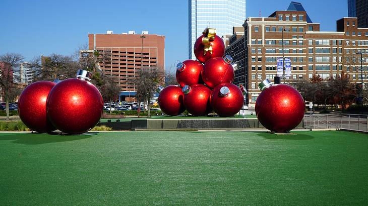 A group of red balls on a grass field with buildings in the background