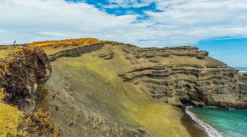 Green sand cliffs with the ocean at the bottom under a blue sky with clouds