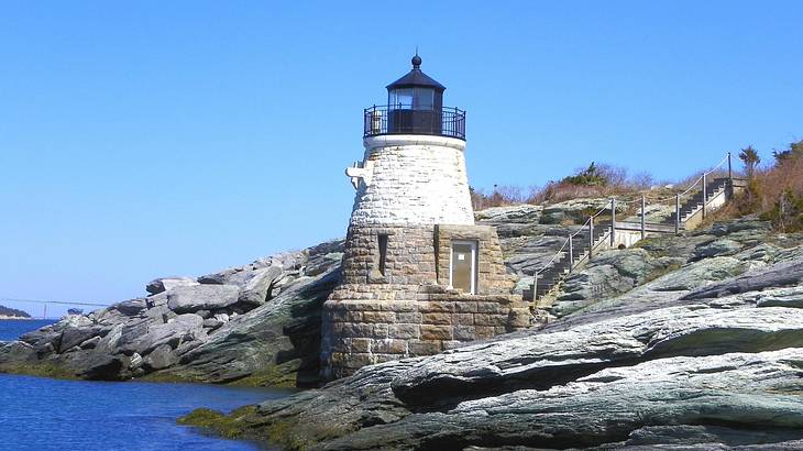 A small lighthouse sitting on the rocks with ocean water to the side