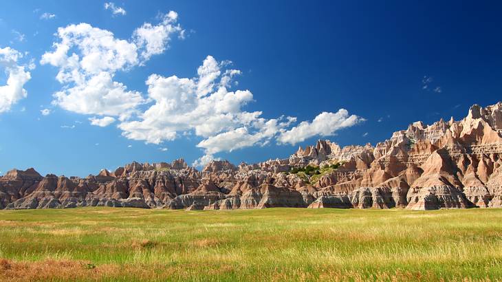 Green grass next to striated rock mountains under a blue sky with clouds