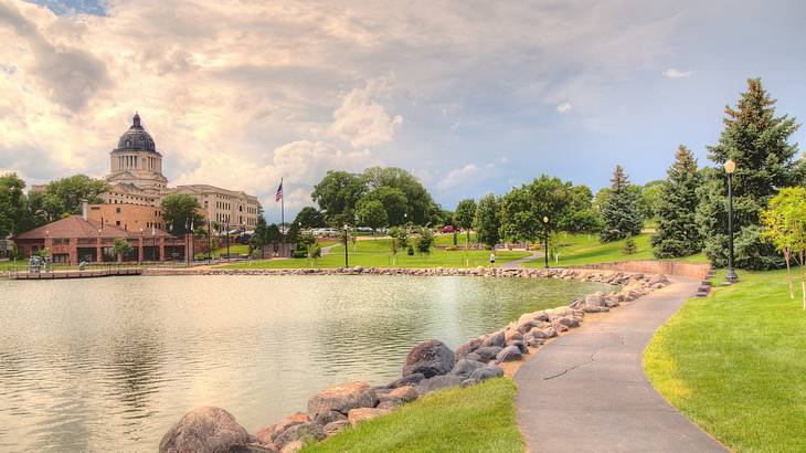 A path past a pond with trees on one side and a state capitol building on the other A path past a pond with trees on one side and a state capitol building on the other