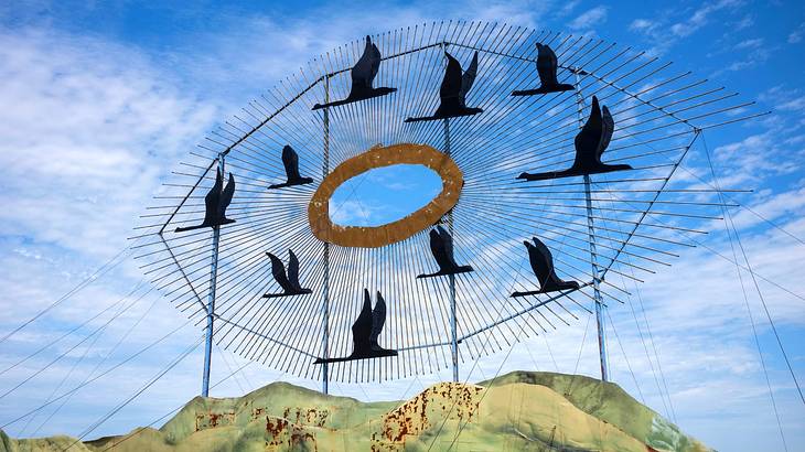 A black sculpture with Geese flying around a circle against a blue sky
