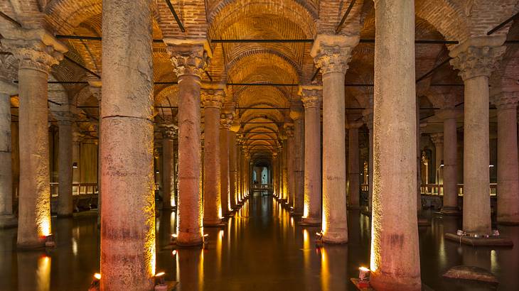 A large illuminated underground room with pillars and water on the ground