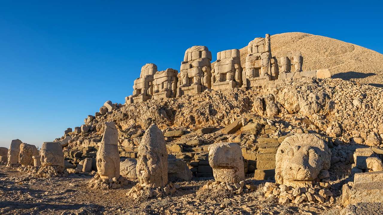 A rocky cliff with many stone statues and ruins next to a clear blue sky