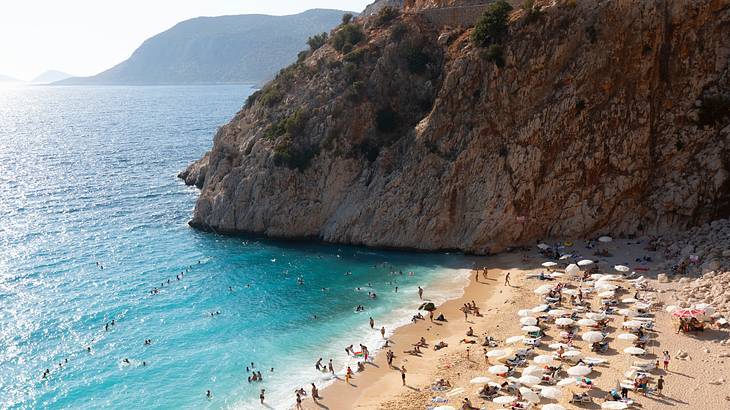 A beach with people on it by a cliff and the bright blue ocean