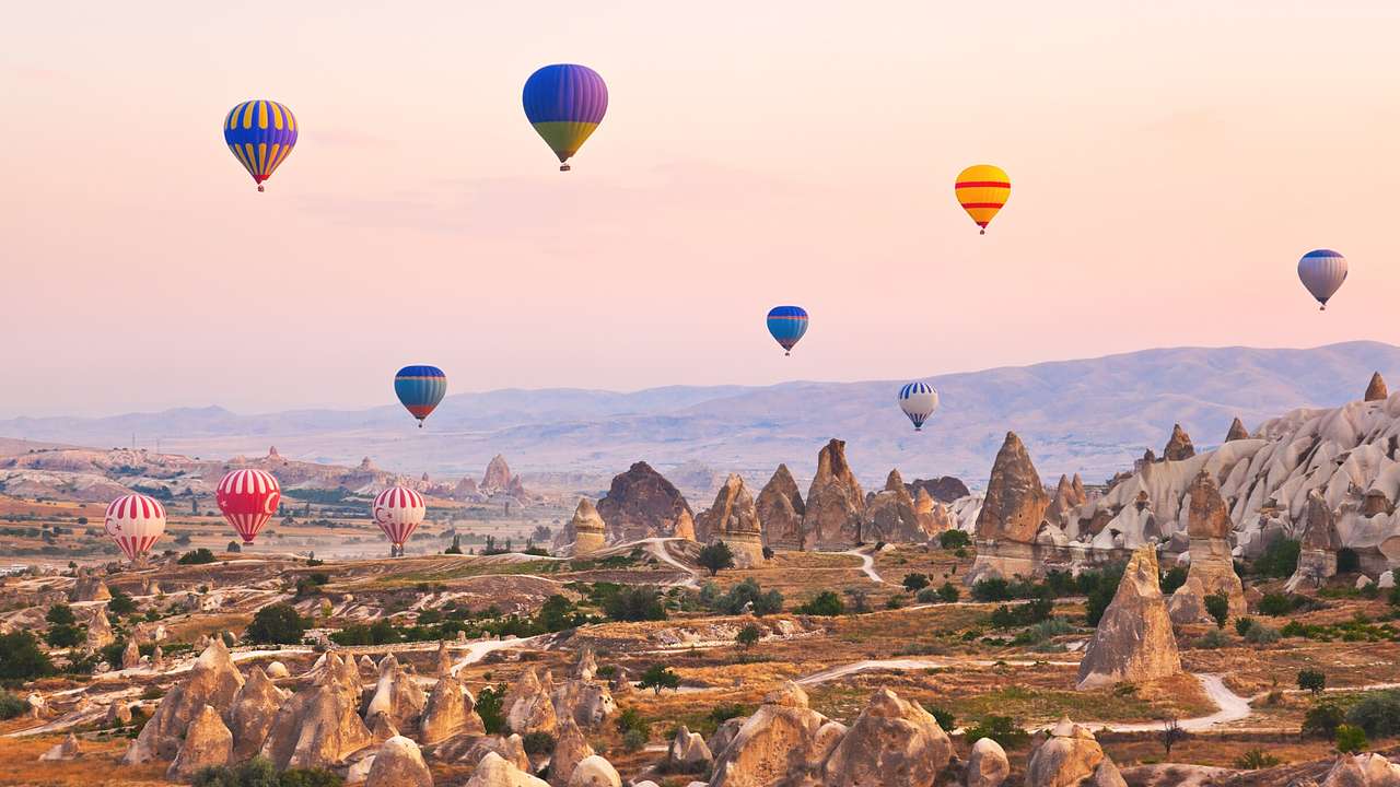 A park with rock formations and colourful hot air balloons in the sky at sunset