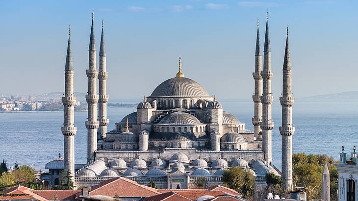 A large building with a dome and six minarets with a body of water behind it